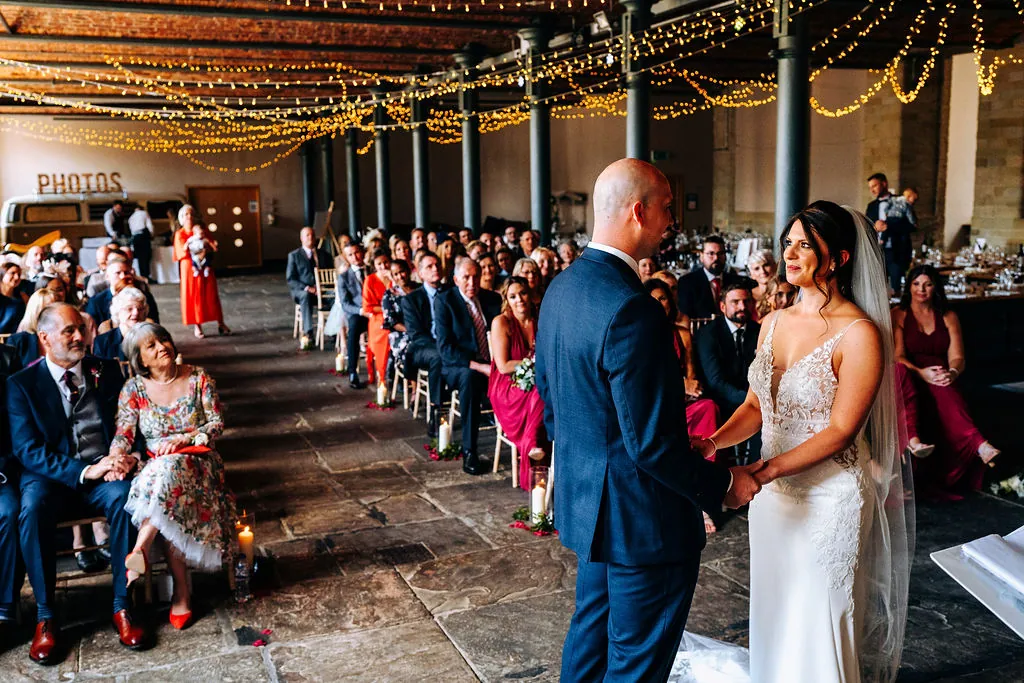 A couple walk back down the aisle between seated guests, cast-iron columns strung with fairy lights