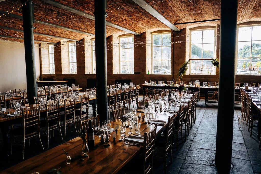 Long wooden tables dressed for a wedding breakfast beneath the vaulted brick ceiling and tall windows